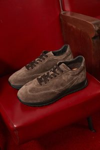 A pair of brown suede sneakers with black soles placed on a red leather chair.